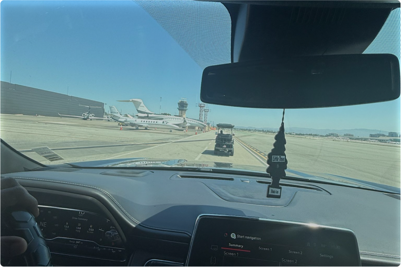 Dashboard view of vehicle at airport with planes visible in the distance